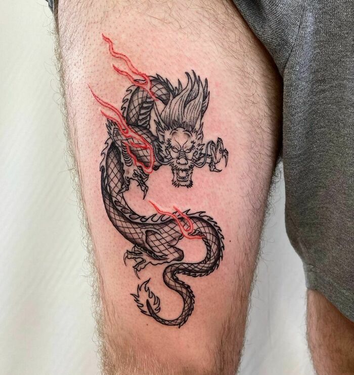 Red ink tattoo design featuring a dragon with red highlights on a person's thigh.