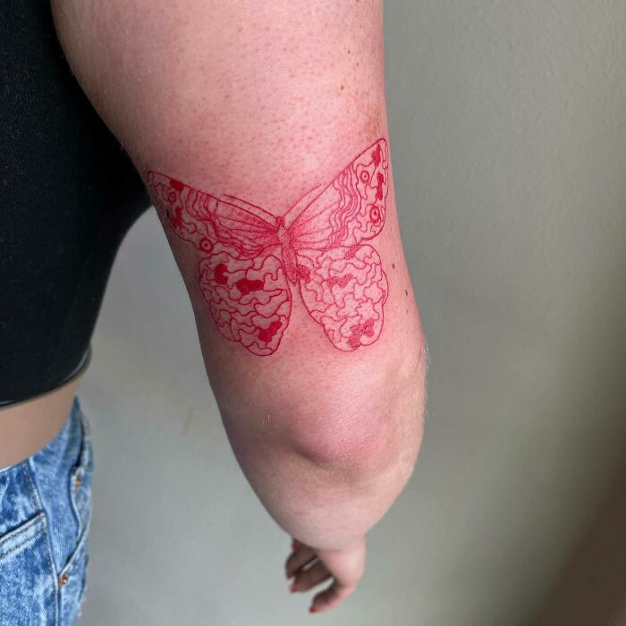 Red ink tattoo of a detailed butterfly design on an arm.
