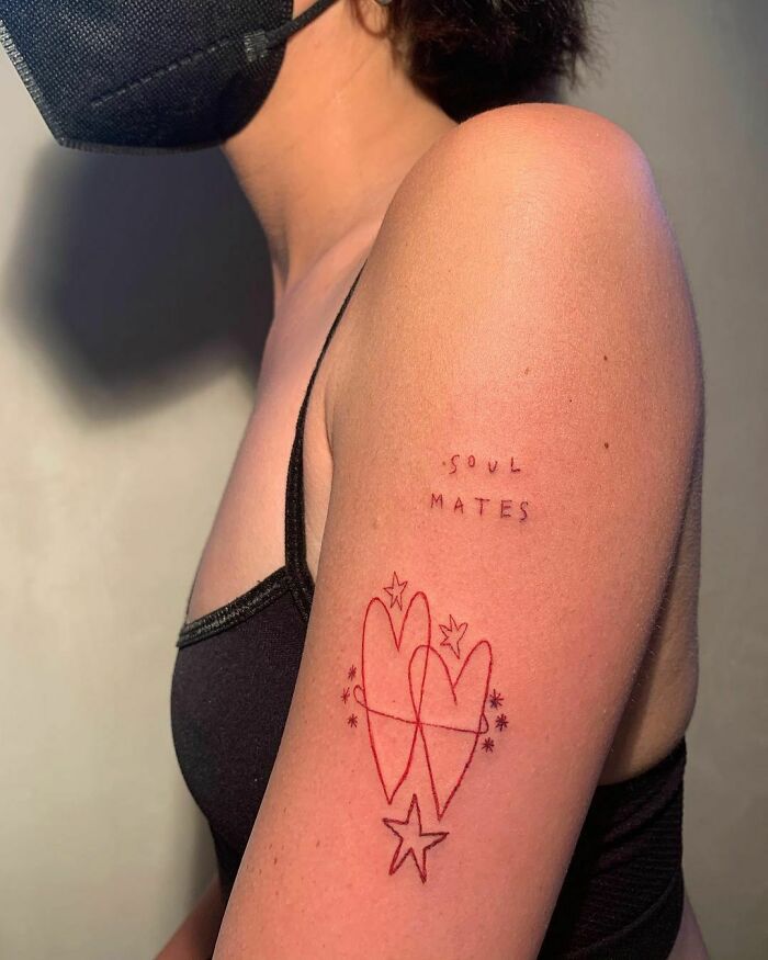 Red ink tattoos of intertwined hearts, stars, and 'soul mates' text on an upper arm.