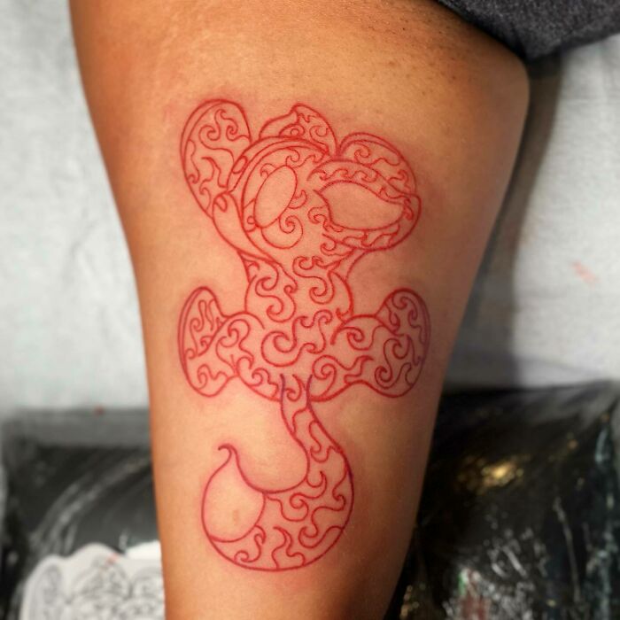 Red ink tattoo featuring intricate swirling patterns on a person's arm.