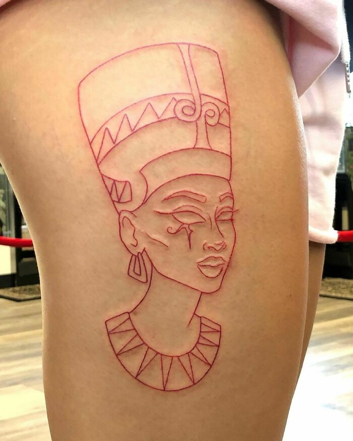 Red ink tattoo depicting an ancient Egyptian queen on a person's thigh.