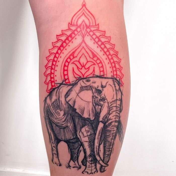 Red ink tattoo featuring an ornate design above a black and gray elephant on a person's arm.