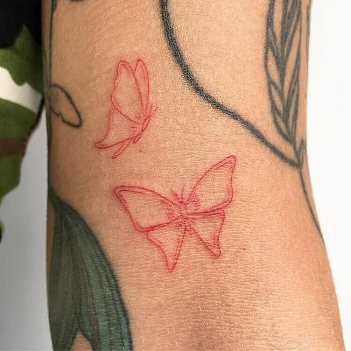 Red ink butterfly tattoo design on skin, showcasing delicate line work and artistic detail.