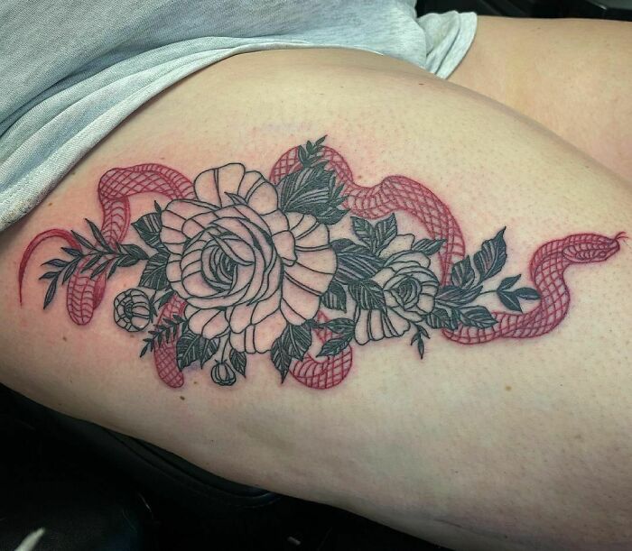Red ink tattoo of roses and a serpent on a thigh, showcasing intricate design elements in a floral and reptilian motif.