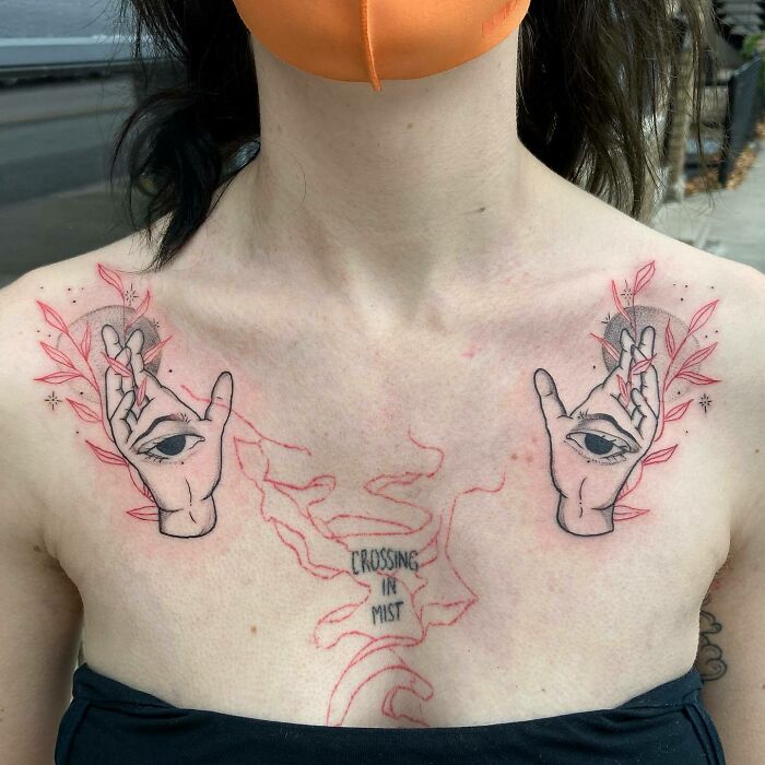 Person with red ink tattoo featuring hands, eyes, and leaves across the chest.