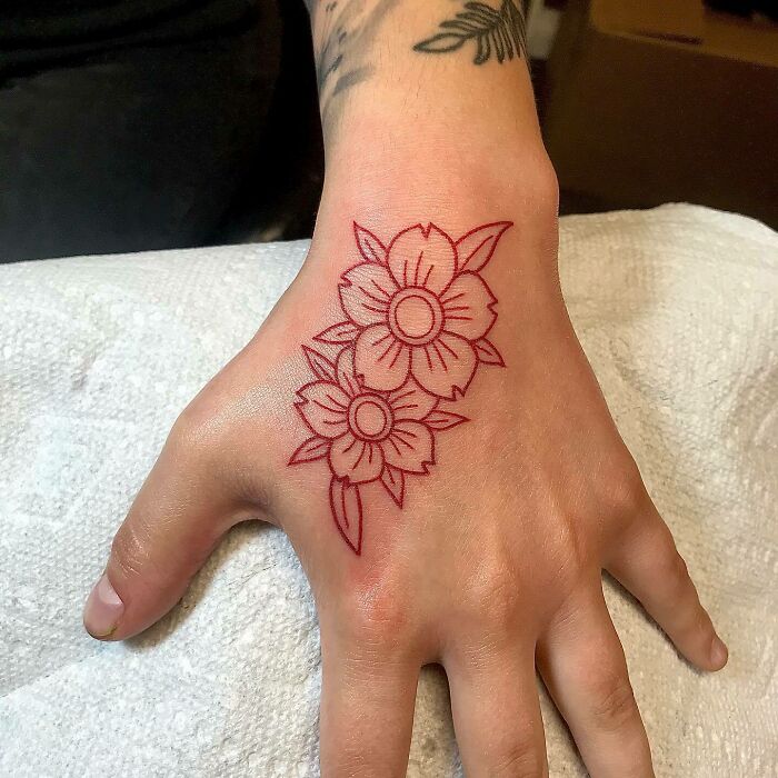 Red ink tattoo of floral design on the back of a hand.