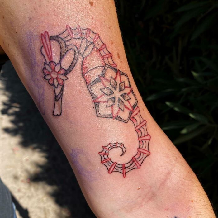 Red ink seahorse tattoo design with floral patterns on forearm skin.