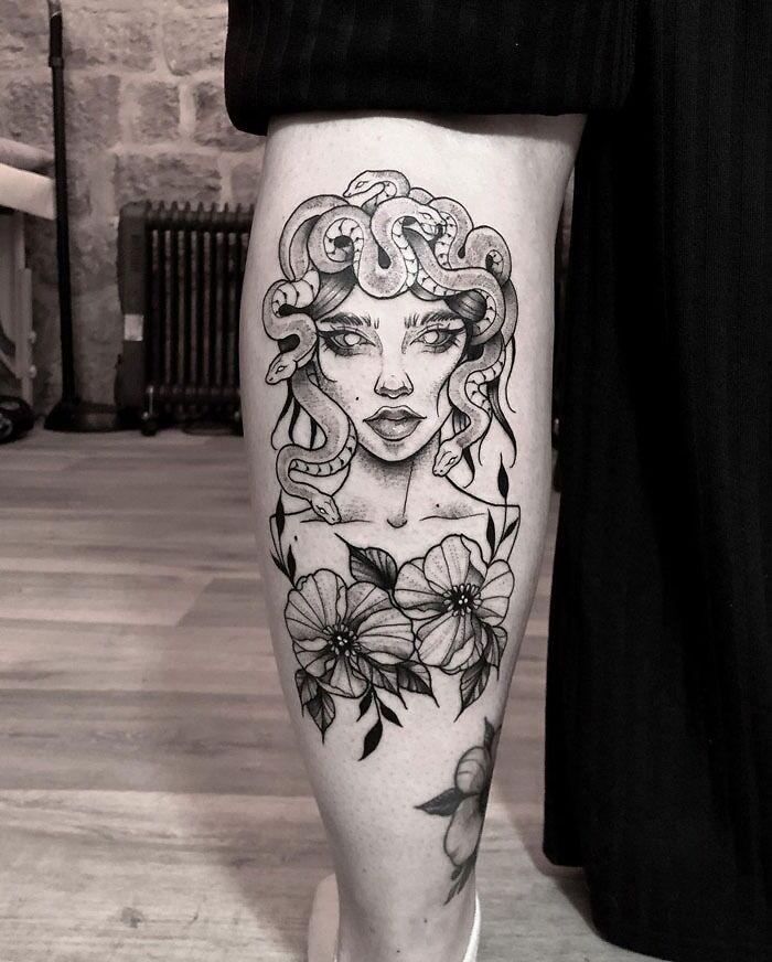 Lower leg tattoo of Medusa with snakes and flowers in black ink.