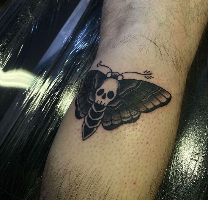 Moth tattoo with a skull design on the lower leg, showcasing bold lines and dark shading.