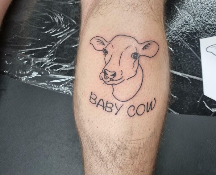 Lower leg tattoo of a baby cow outline on a person's calf.