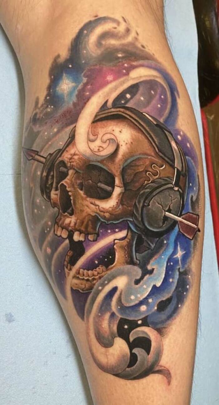 Lower leg tattoo featuring a colorful cosmic skull with headphones.