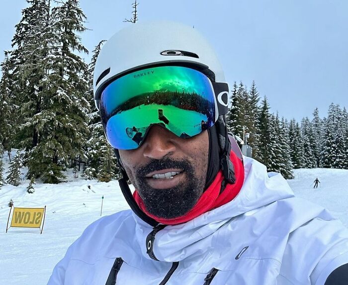 Man in ski gear with mirrored goggles on a snowy mountain, smiling at the camera.