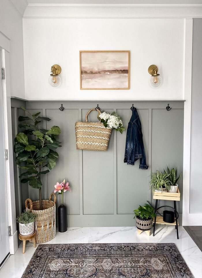 Wall with creative decoration ideas: green paneling, plants, woven basket, denim jacket, framed artwork, and wall sconces.