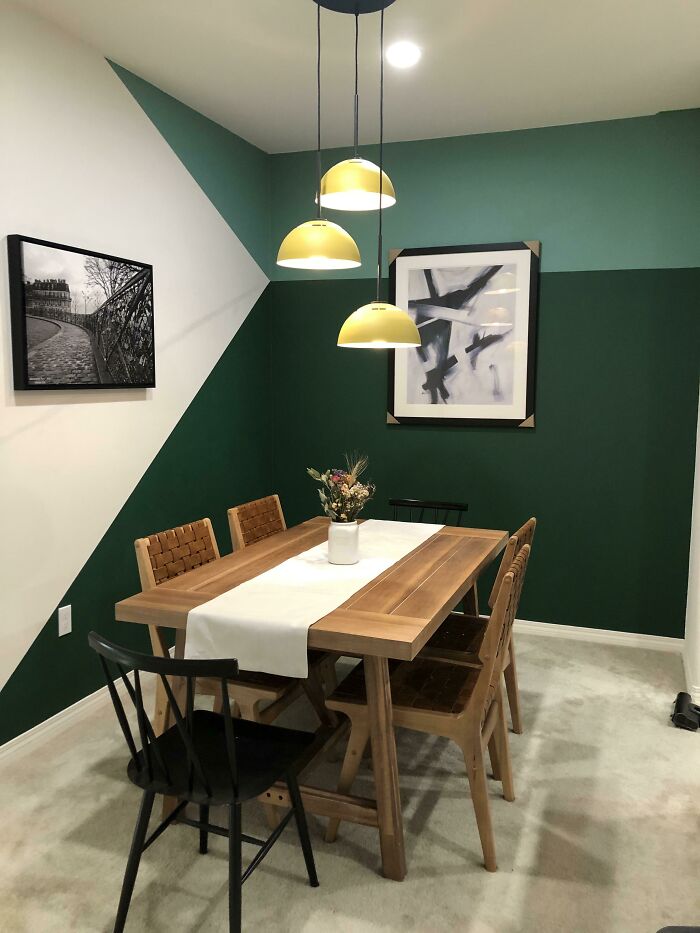 Dining area with green accent wall, wooden table, mixed chairs, and yellow pendant lamps for creative decoration ideas.