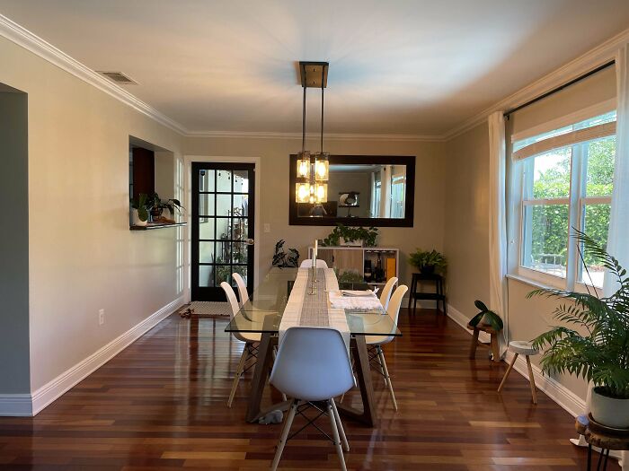 Dining room with wooden floor, glass table, white chairs, and potted plants, showcasing home decoration ideas.
