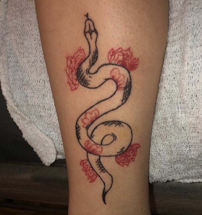 Red ink snake tattoo intertwined with roses on skin, showcasing delicate artistry and bold design.