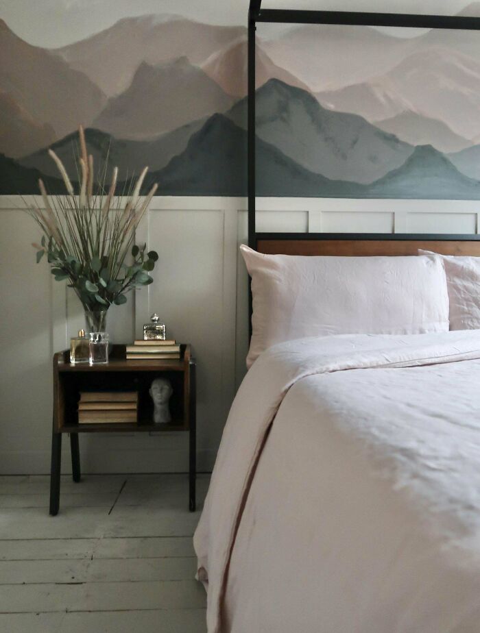 Cozy bedroom with creative decoration, featuring a mountain mural, side table with books and a vase.