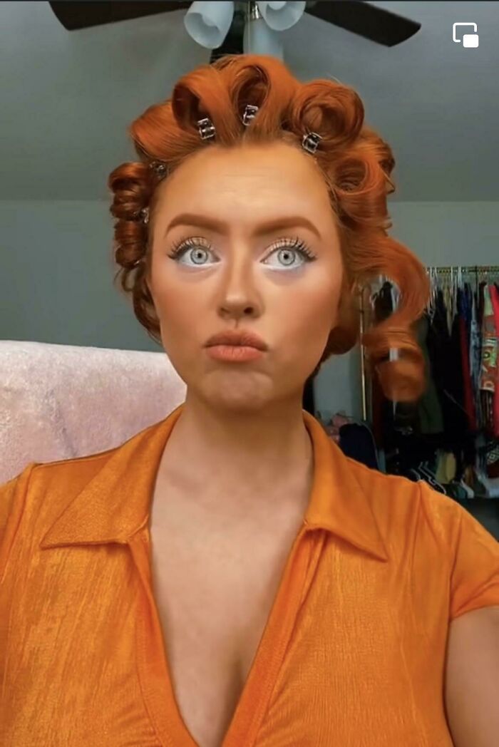 Person with exaggerated makeup, featuring bright orange blush and lipstick, in a colorful top; makeup fail.
