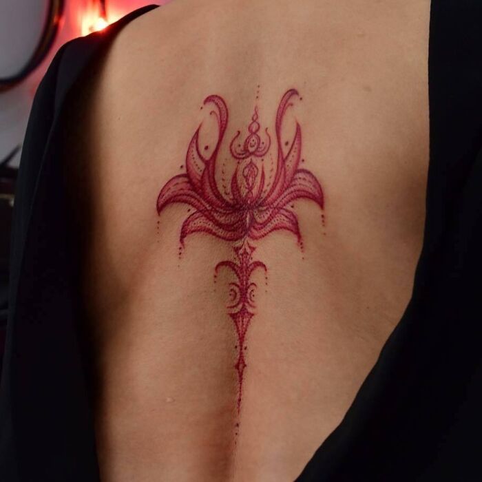 Elegant red ink tattoo design with intricate patterns on a person's upper back.
