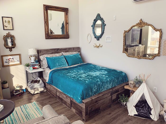 Creative bedroom decoration with teal bedding, ornate mirrors, rustic frames, plant decor, and a small decorative teepee.