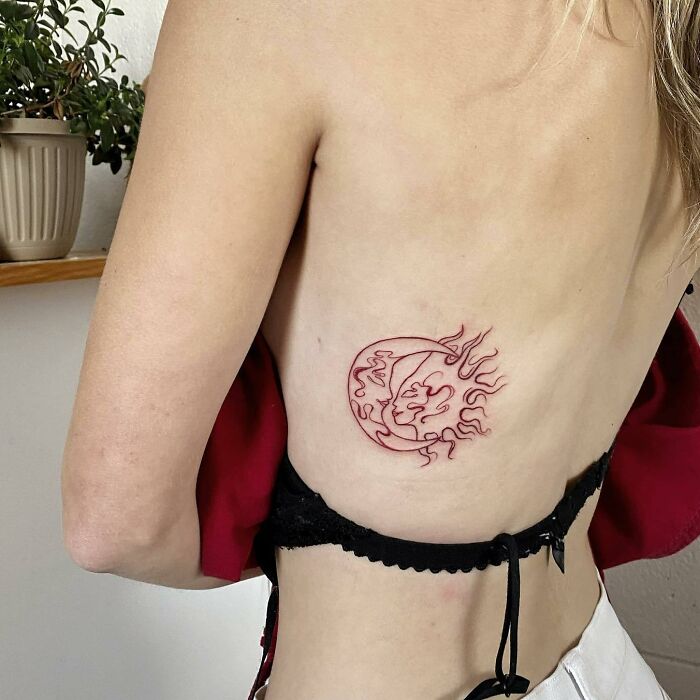 Red ink tattoo of a sun and moon design on person's side, showcasing intricate detailing.