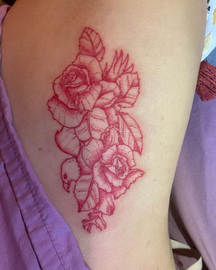 Red ink tattoo of roses and leaves on an arm, showcasing intricate line work.