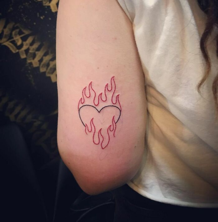 Red ink tattoo of a heart with flames on an arm, showcasing a creative tattoo design.
