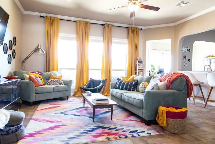 Cozy living room with colorful decor, featuring blue sofas, yellow curtains, and a vibrant geometric rug for creative inspiration.