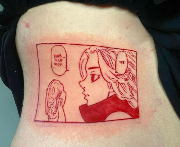 Red ink tattoo of anime character with speech bubbles, lines and shading detail, designed on a person's side.