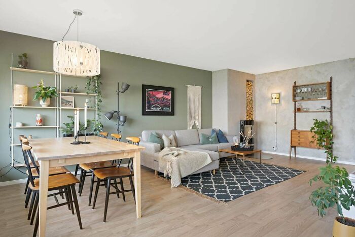 Modern home decoration with green accent wall, gray sofa, wooden dining set, and plants enhancing the cozy living space.