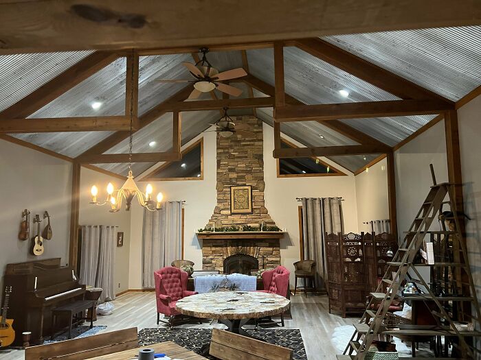 Spacious living room with creative decoration ideas, featuring stone fireplace, chandelier, and rustic wooden beams.