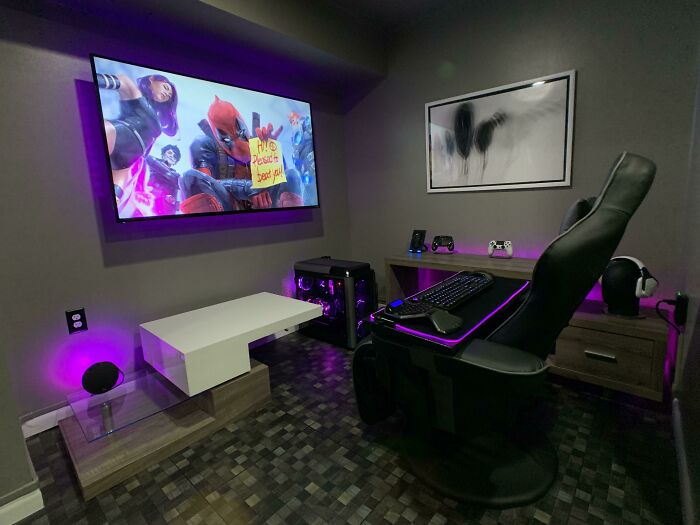 Gaming room setup with modern decoration ideas; features a purple-lit desk, sleek chair, and large wall-mounted screen.