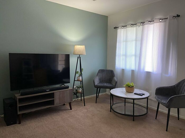 Cozy living room with modern decor, featuring a TV, lamp, chairs, and coffee table.