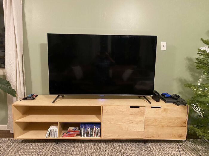 TV on wooden stand with home decoration items; game controllers and books.
