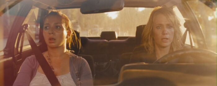 Two women in a car, showcasing iconic best friend duos, looking surprised while driving at sunset.