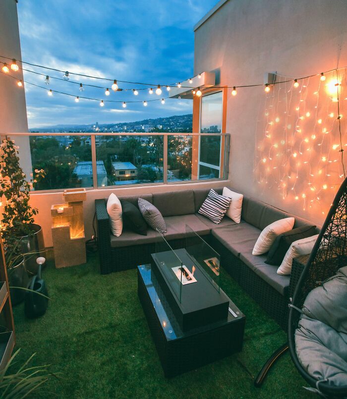 Rooftop patio with creative decoration, featuring string lights, a cozy sectional sofa, and a city view.
