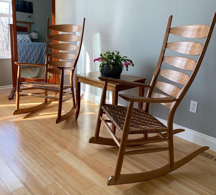 Two wooden rocking chairs with woven seats and a table with a potted plant for home decoration.
