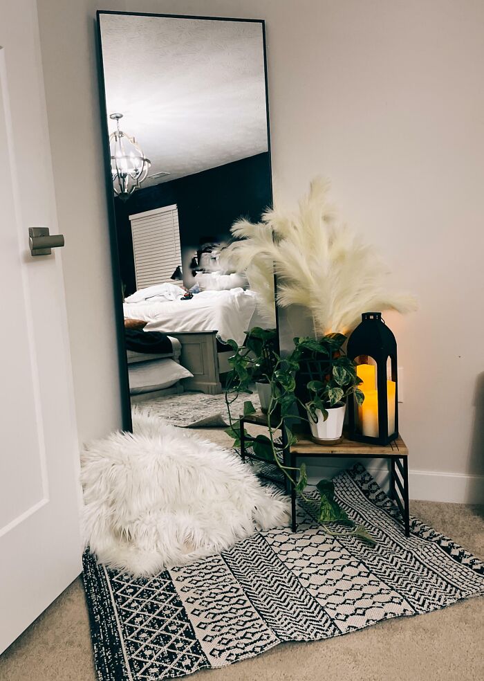 Home decoration idea with a large mirror, cozy rug, fluffy pillow, potted plant, and decorative lantern in a stylish room.