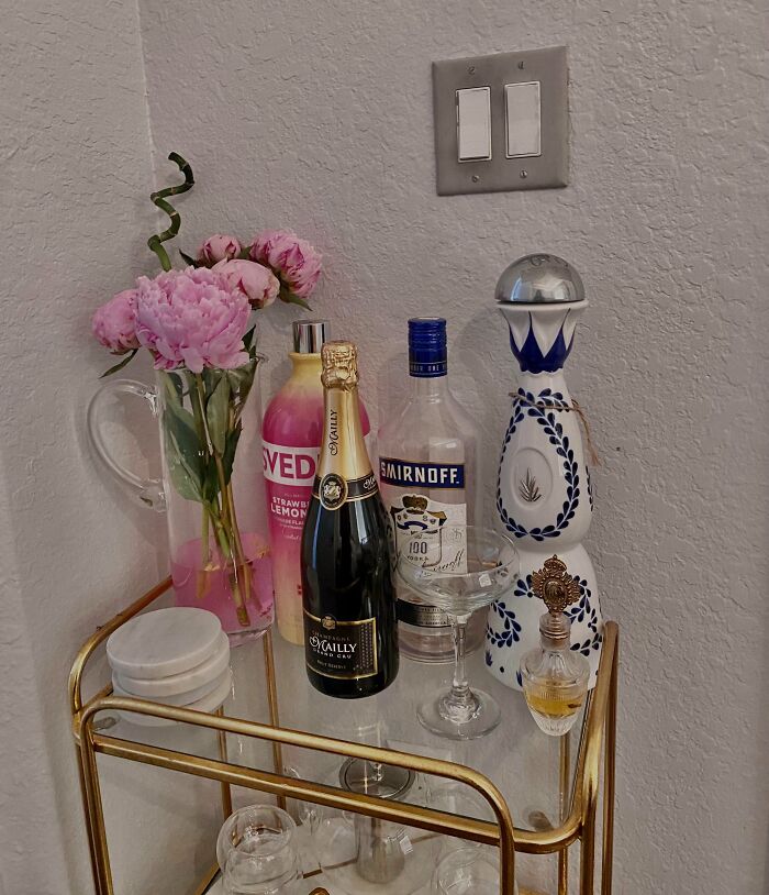 Creative decoration inspiration with a gold bar cart, pink flowers, and assorted bottles.