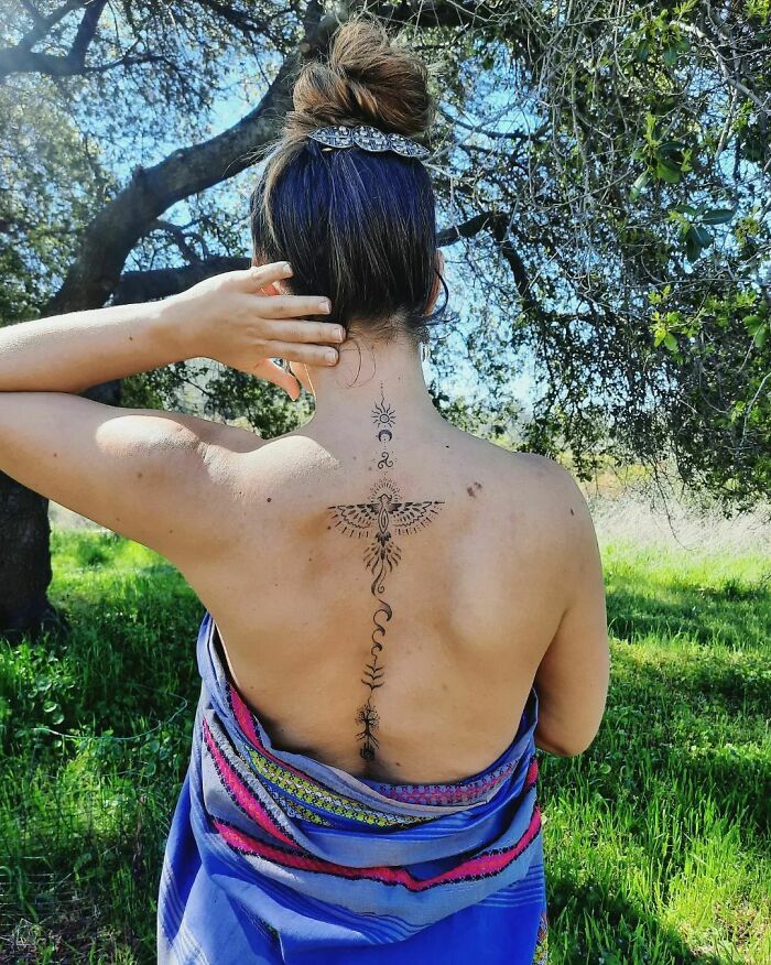 Woman with elegant spine tattoo posing outdoors, wrapped in blue fabric.