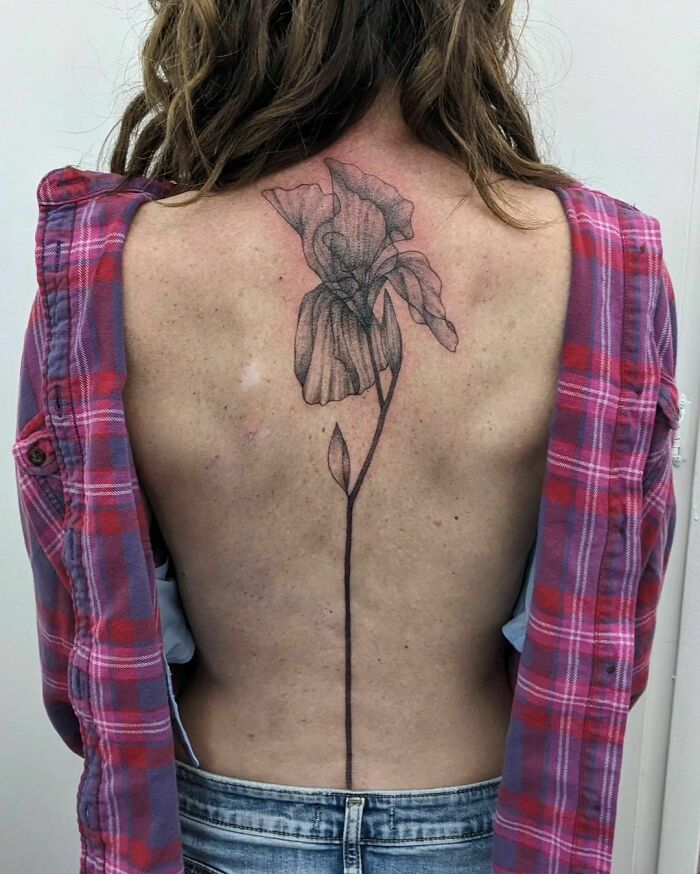 Detailed flower spine tattoo on woman's back, wearing a plaid shirt.