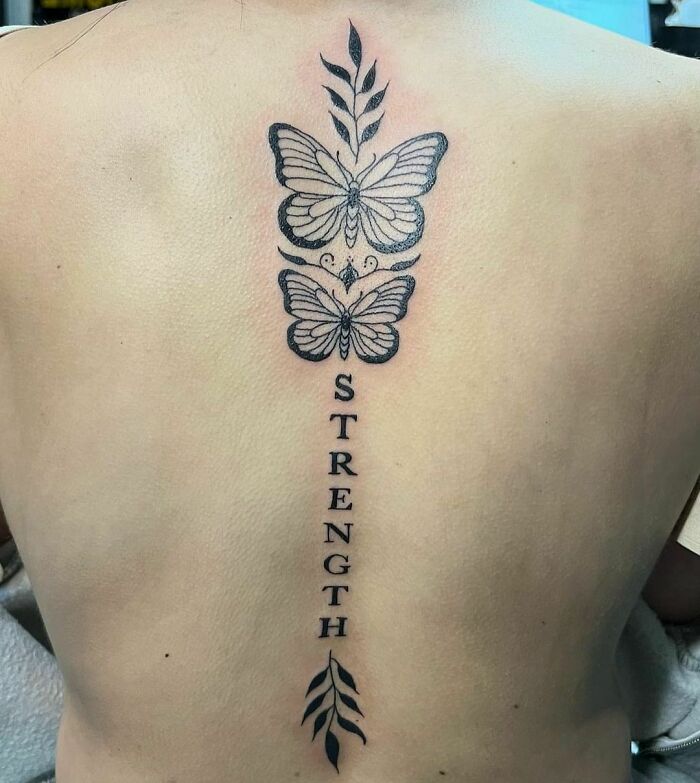 Butterfly spine tattoo with the word "strength" and decorative leaves, showcasing elegant tattoo ideas.