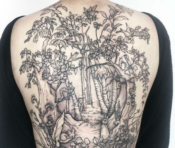 Back tattoo of a detailed forest scene, featuring trees, leaves, and wildlife in a nature-inspired design.
