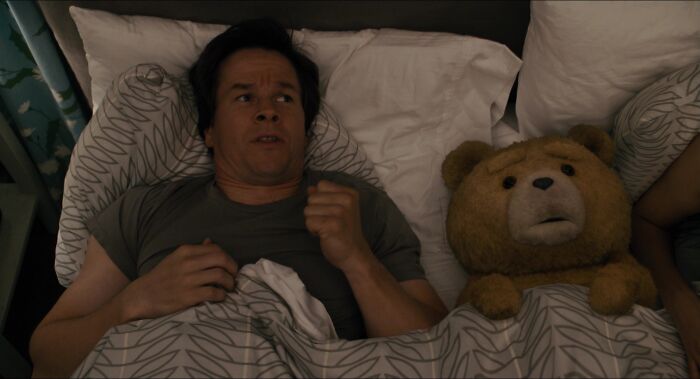 A man lying in bed next to a teddy bear, symbolizing iconic best friend duos in a cozy setting.