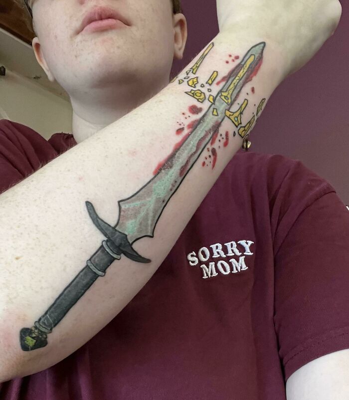 Forearm with a detailed sword tattoo and "Sorry Mom" shirt, showcasing unique wrist tattoo ideas.