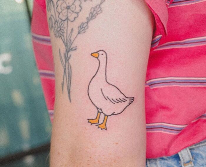 Animal tattoo of a goose on an arm with floral designs, against a pink striped shirt background.