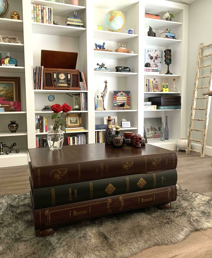 Home decoration with stacked book table, red roses, and eclectic shelf decor.