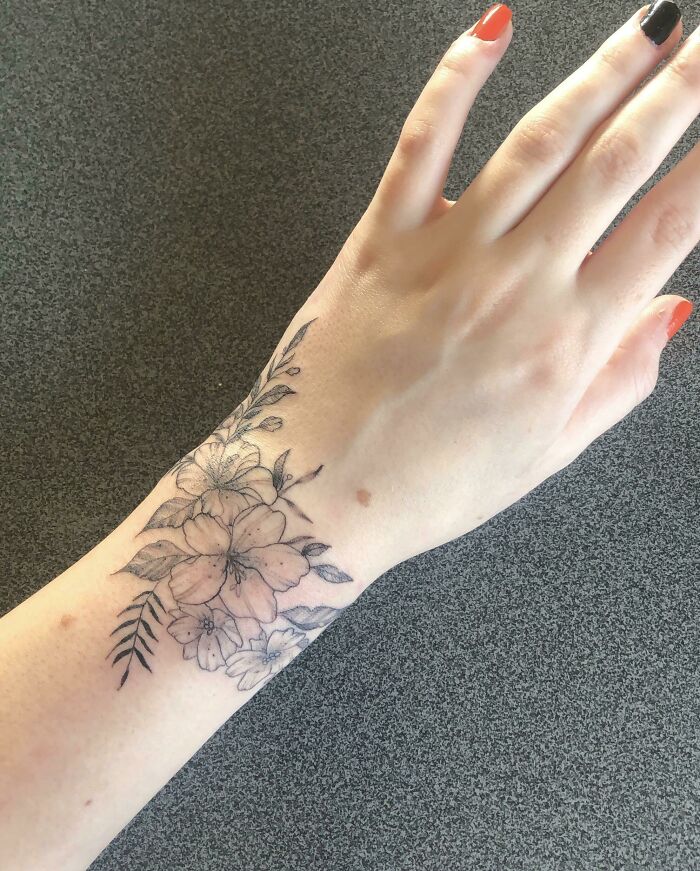 Floral wrist tattoo with delicate blossoms and leaves, showcasing timeless style on a light-skinned hand.