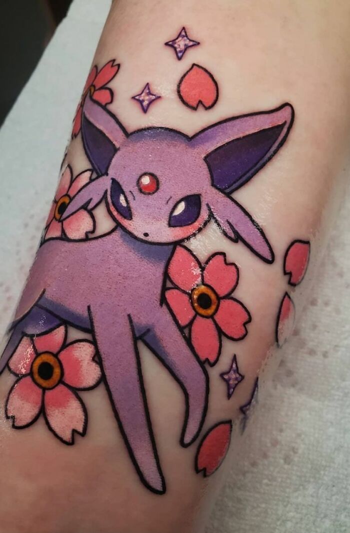 Purple Espeon wrist tattoo with pink flowers and stars.
