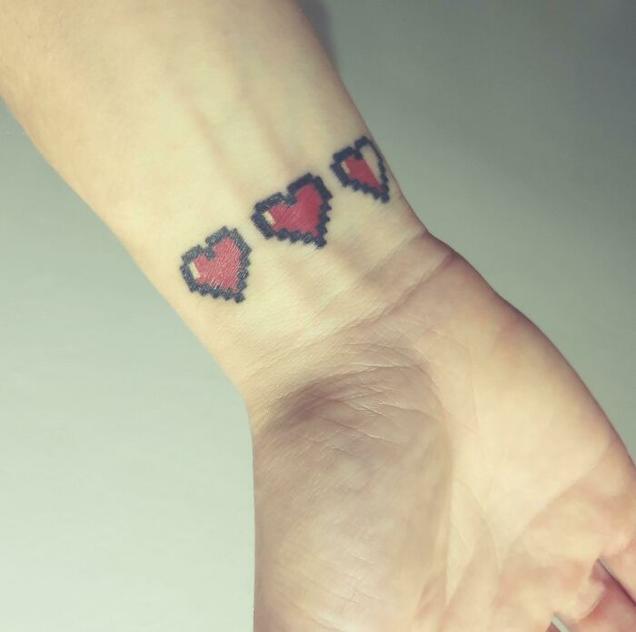 Pixelated heart wrist tattoo design featuring three small red hearts.